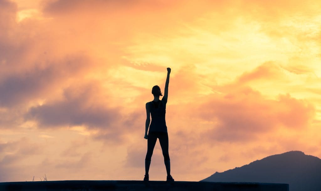 Woman holding up fist in power at sunset